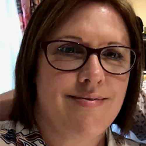 A person with brown hair in a mid length style smiles at the camera