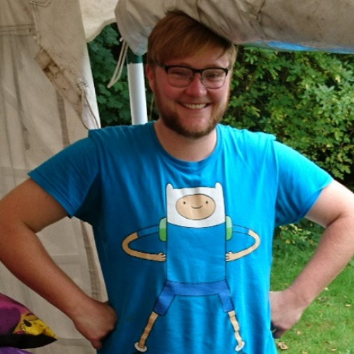 A smiling person with glasses and a short cropped beard stands inside a marquee